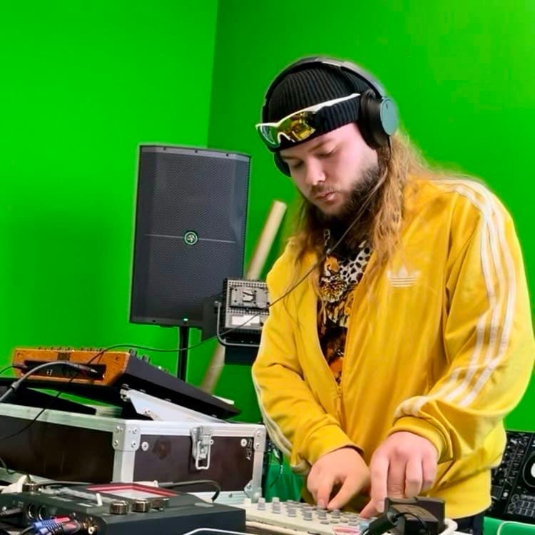 Hlib Dovzhuk DJing on a green-screen set, yellow jacket and headphones